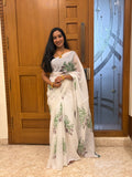 Woman in a white dress with green patterns standing in front of a wooden door.